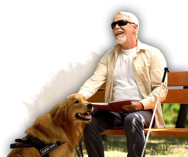 Man with white cane and glasses sitting on a bench. A service dog sits at his feet.